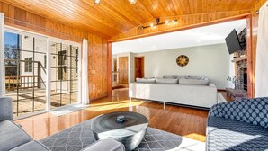 A spacious living area with a wooden ceiling, a grey sofa, a patterned sofa, and a coffee table.