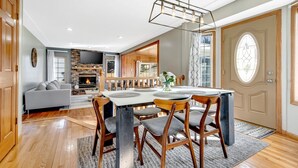 A modern living room with a fireplace, a dining area with a table and chairs, and a large window with curtains.
