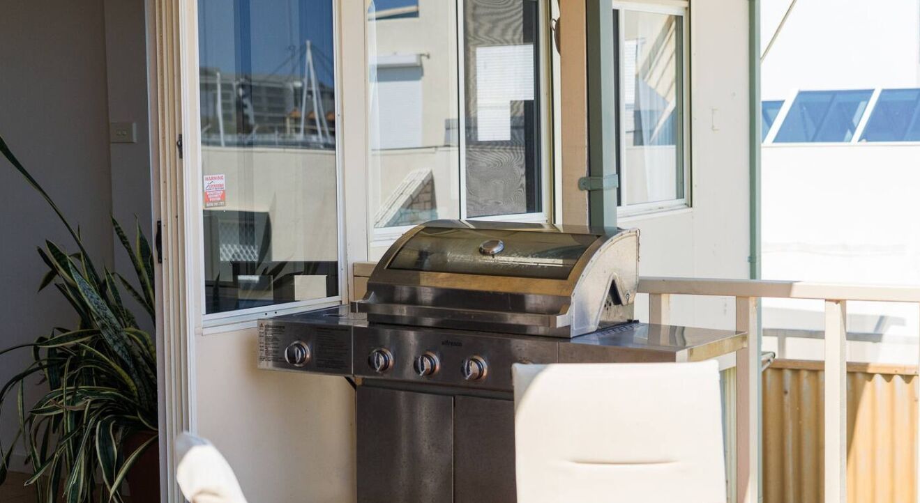 A compact kitchen with a built-in grill, a white chair, and a potted plant.