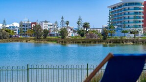 A waterfront view with a chair by the water, a metal fence, and modern buildings in the background. - Mandurah Overlooking The Marina (Mandurah)