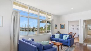 A living room with a large window, a blue sofa set, and a view of a lake. - Mandurah Overlooking The Marina (Mandurah)