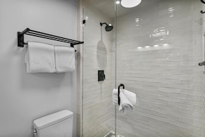 Et moderne badeværelse med en glasbrusekabine, toilet og håndklæderække.