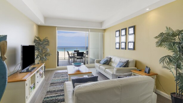 Ein Wohnzimmer mit Sofa, Couchtisch, Fernseher und Blick auf den Strand.