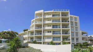 Ein mehrstöckiges Hotel mit Balkonen, umgeben von gepflegten Gärten und Palmen.