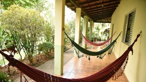 A hammock under a covered patio with tiled flooring and potted plants.