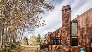 A modern wooden house with a chimney, a front porch, and a yard with fallen leaves. - Exquisitely appointed-2BR+Loft-walk to Three Kings lift with private hot tub (Park City)