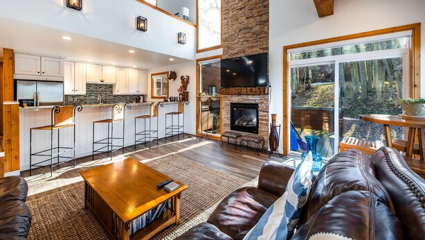 A spacious living area with a fireplace, a kitchen with high ceilings, and large windows offering a view of the outdoors. - Exquisitely appointed-2BR+Loft-walk to Three Kings lift with private hot tub (Park City)