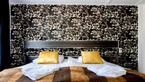Een hotelkamer met een groot bed, twee kussens, een hoofdeinde en een muur met een bloemenmotief.