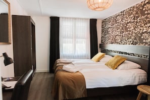 A hotel room with a bed, a desk, a chair, a lamp, and a large window with curtains. - Hanze Hotel Zwolle (Zwolle)