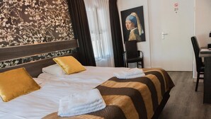 Een hotelkamer met een tweepersoonsbed, twee kussens, een bureau met stoel en een schilderij aan de muur.