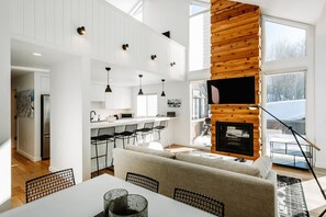 Una cocina moderna con armarios blancos, un comedor con mesa y sillas blancas, y una zona de estar acogedora con un sofá.