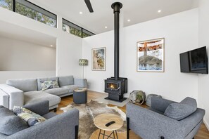 Een moderne woonkamer met een open haard, grijze banken, een salontafel en kunstwerken aan de wanden.