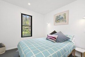 Ein Schlafzimmer mit einem Bett, einem Fenster, einem Gemälde und einem Nachttisch.