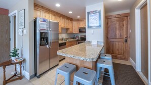 Une cuisine moderne dotée de plans de travail en granit, d’appareils électroménagers en acier inoxydable, d’armoires en bois et d’un îlot central avec des tabourets de bar.