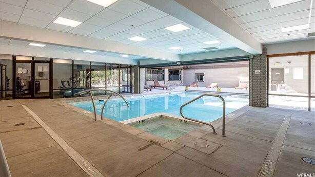 Une piscine intérieure avec des parois en verre transparent, un sol carrelé et un plafond équipé de néons.