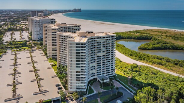 Een hoog hotel met een gebogen gevel, een parkeerplaats en uitzicht op het strand.
