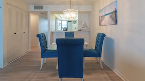 Uma sala de jantar com mesa de vidro e cadeiras estofadas azuis, um candelabro e uma pintura na parede.