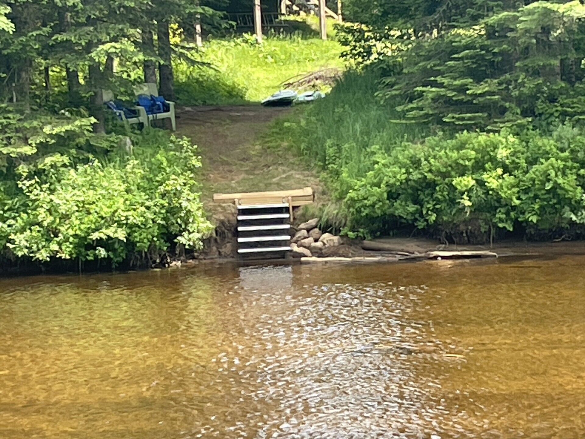 A wooden bridge over a calm river with greenery on both sides.
