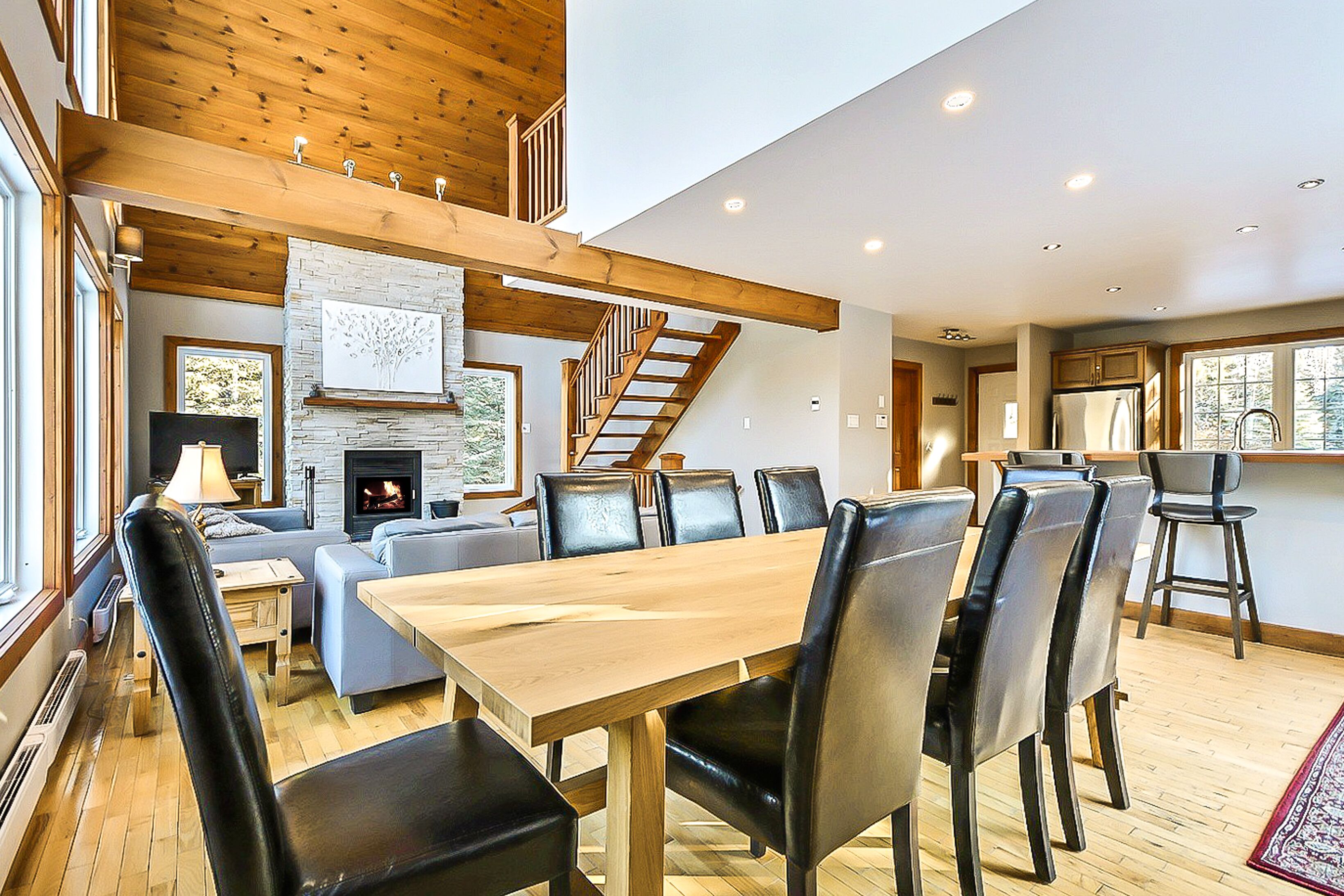 A spacious living area with a fireplace, wooden ceiling, and a dining table with chairs.