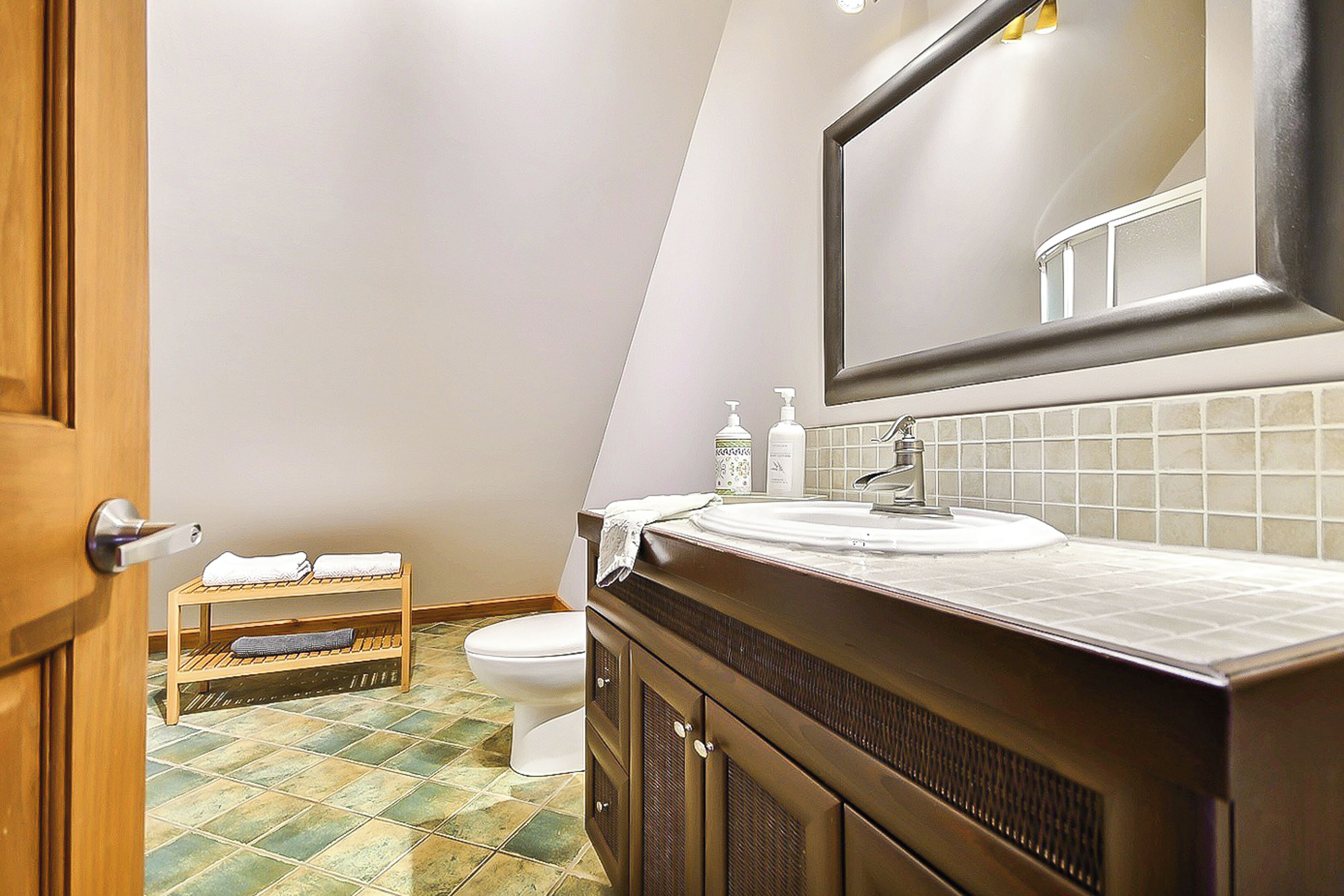 A bathroom with a wooden vanity, a large mirror, a toilet, and a shelf with towels.