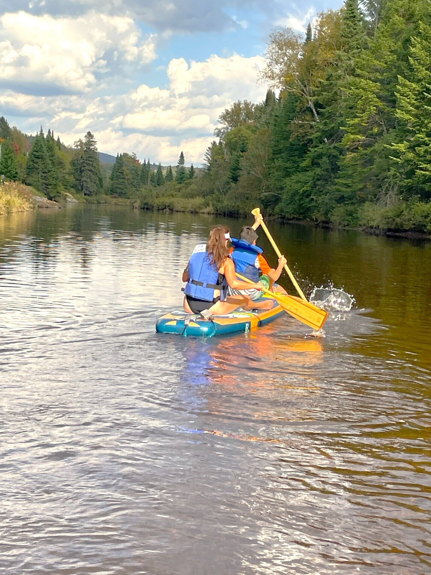 A person paddling a kayak on a calm river surrounded by dense forest.