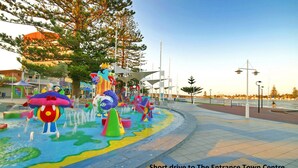 Une fontaine d’eau aux couleurs vives, avec différentes formes, et un chemin menant au centre-ville.
