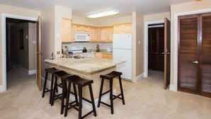 Una cocina con una isla central, armarios de madera, un refrigerador blanco y un microondas. Hay tres taburetes alrededor de la isla.