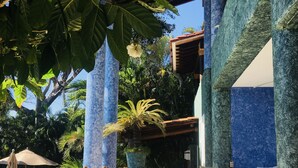 An outdoor seating area with wooden chairs and a wicker table, surrounded by blue columns and a palm tree. - Exclusive Villa with Private Beach and Beautiful  Views to the Pacific Ocean (Bahías de Huatulco)