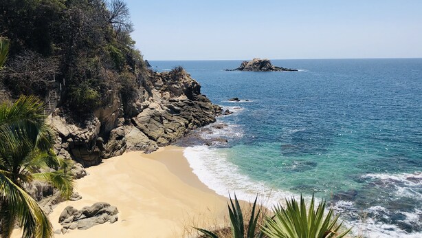 A coastal landscape with a sandy beach, rocky cliffs, and a small island in the distance. - Exclusive Villa with Private Beach and Beautiful  Views to the Pacific Ocean (Bahías de Huatulco)