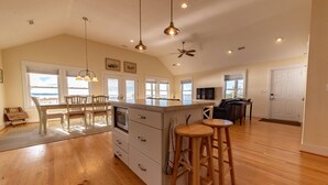 A spacious kitchen with a large island, wooden bar stools, and a view of the ocean through large windows. - Sunset Joy - KDH MP 6, Soundfront, Sound View, Kayak, Community Boat Ramp, Pets OK, Flex Stays (Kill Devil Hills)