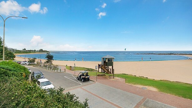 Une plage avec une vue sur un poste de surveillance des sauveteurs, un espace de stationnement et un ciel dégagé.