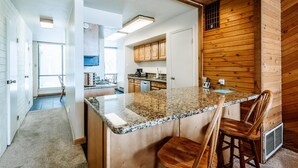 A modern kitchen with granite countertops, wooden cabinets, and a central island with bar stools. - Nostalgic Park City 2BR+Loft-Gas Fireplace-Walk to Park City Resort-In Unit W/D (Park City)