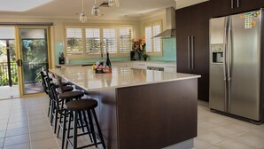 Een moderne keuken met een groot eiland, donkere kastjes, roestvrijstalen apparatuur en een bar met krukken.