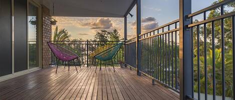 A wooden deck with two hammocks, a balcony railing, and a view of trees and sky.