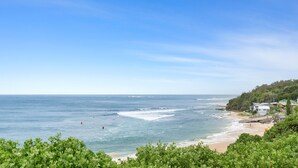 A coastal view with a beach, ocean waves, and a hillside with buildings.
