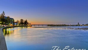 A waterfront area with a bridge, buildings, and a calm water body reflecting lights.