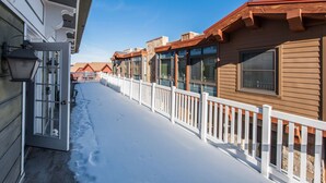 En snötäckt utomhuskorridor med vita räcken och en träbyggnad med stora fönster.