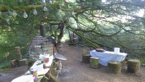 An outdoor dining area with a stone oven, wooden tables, and benches.