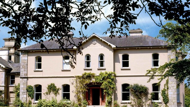 A two-story building with a symmetrical facade, a central entrance with a red door, and a stone base.