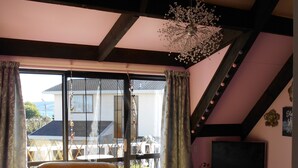 Ein Zimmer mit großem Fenster, einem Bett mit floralem Überwurf und einer Chandelüster.