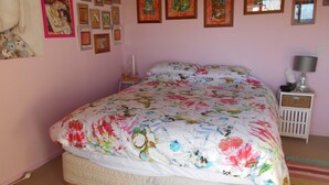 Ein Schlafzimmer mit einem floralen Bettüberwurf, einem Nachttisch mit Lampe und einer mit gerahmten Bildern dekorierten Wand.