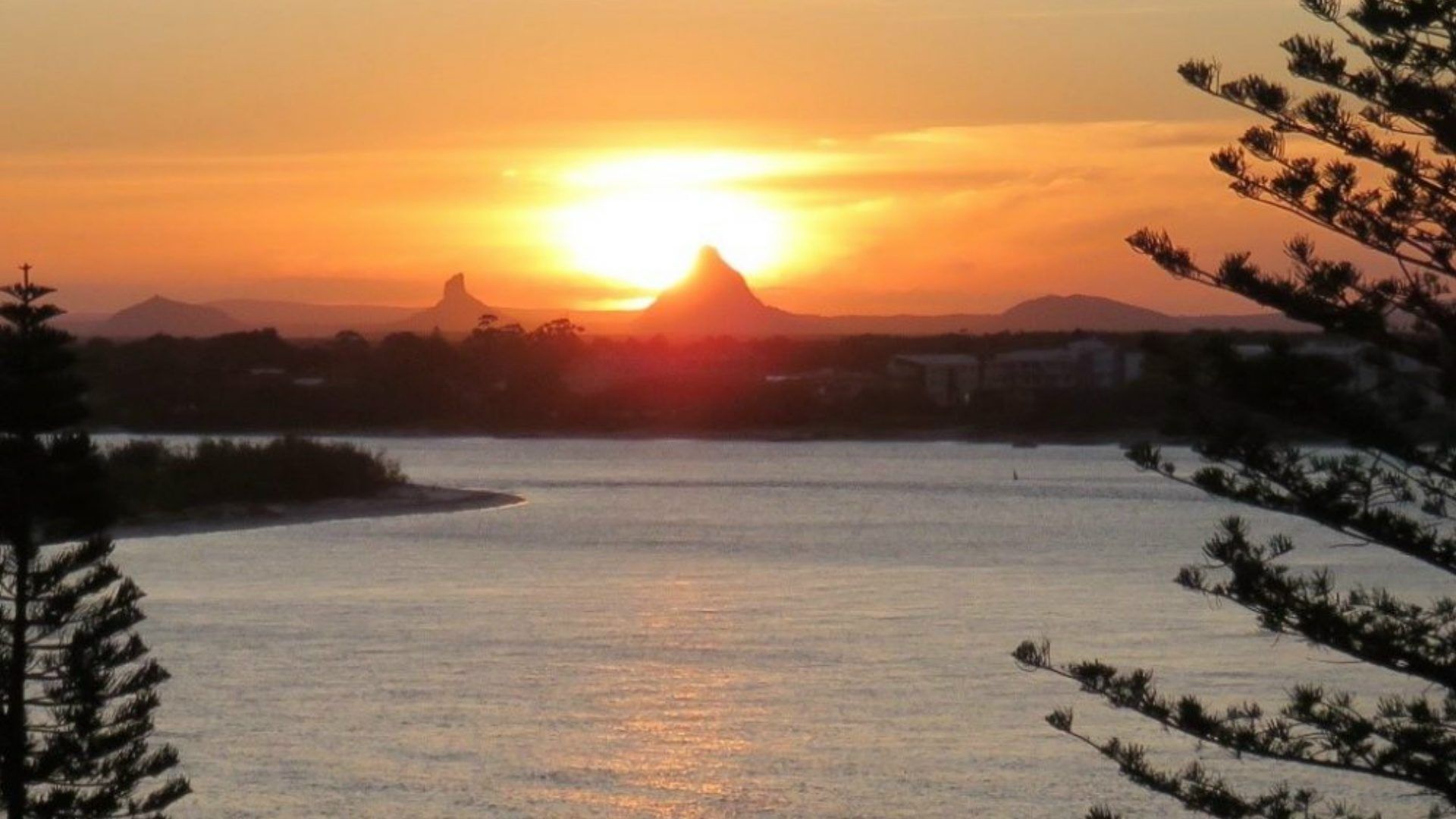Un atardecer sobre un río tranquilo con una montaña al fondo.