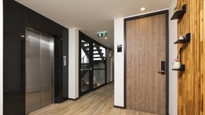 A modern hallway with a wooden floor, a glass elevator, and a wooden door. - Sukhon Hotel (Bangkok)