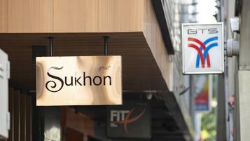 A sign for 'Sukhon' in a commercial area with a BTS station sign in the background.