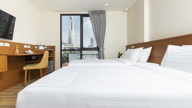 A hotel room with a large bed, a desk, a chair, a TV, and a city view. - Sukhon Hotel (Bangkok)