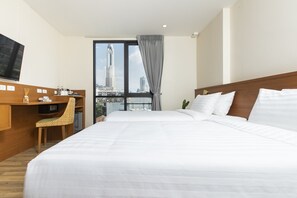 A hotel room with a large bed, a desk, a chair, a TV, and a city view. - Sukhon Hotel (Bangkok)