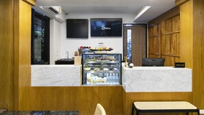 A hotel reception area with a marble counter, a glass display case with snacks, a Dell computer, and a 'Check-In' sign. - Sukhon Hotel (Bangkok)
