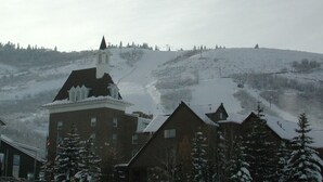 Ein schneebedecktes Wohngebiet mit einem markanten Gebäude, vermutlich eine Kirche oder ein Gemeindehaus, und einem Hügel im Hintergrund, auf dem ein Skilift zu sehen ist.