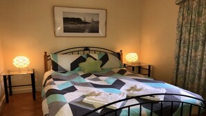 Una cama bien hecha con colcha de estampado geométrico, dos lámparas de noche, un cuadro en la pared y una ventana con cortinas.