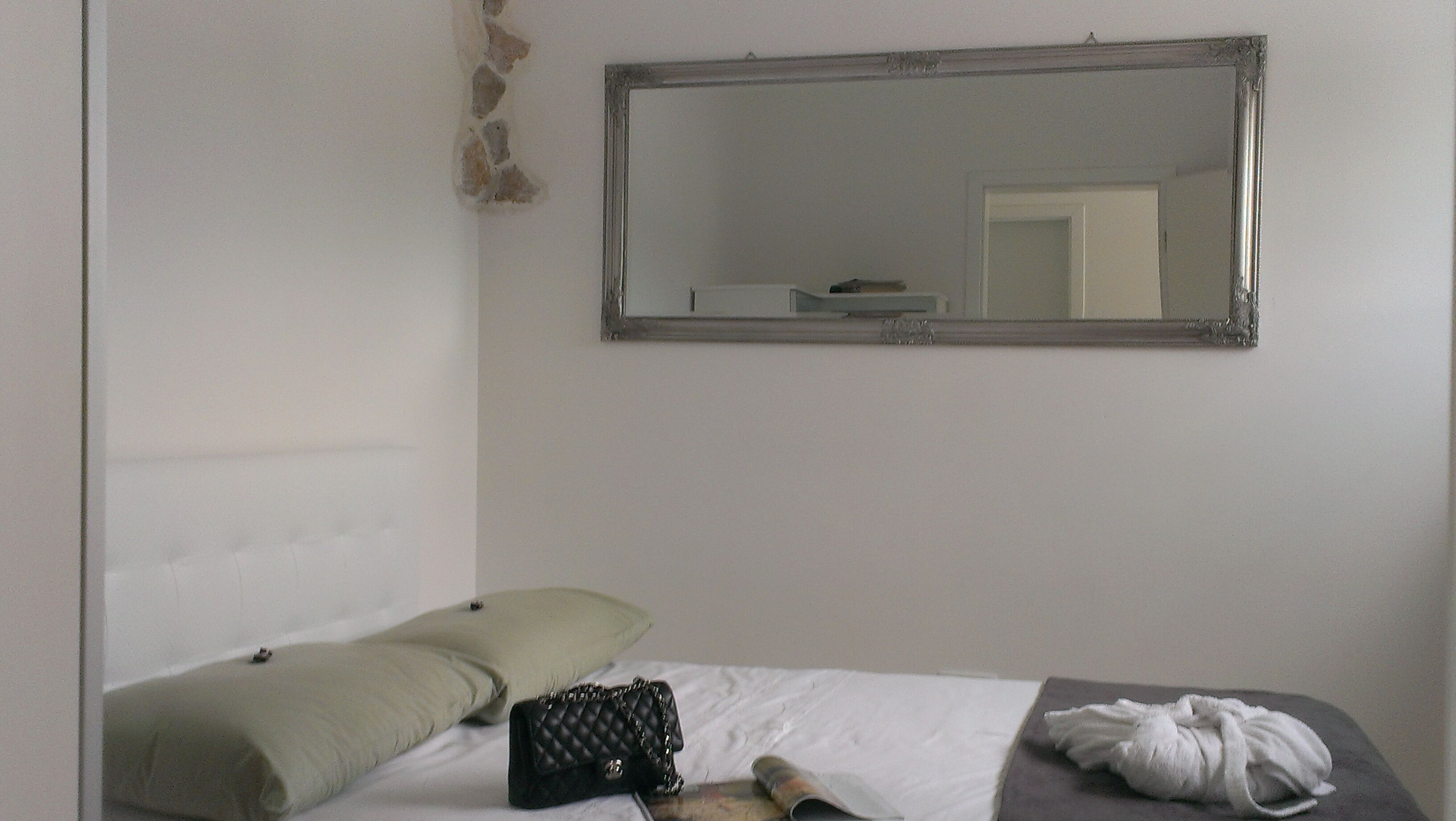 Une pièce simple, avec un lit, un oreiller, un sac matelassé, une serviette blanche et un miroir au mur.